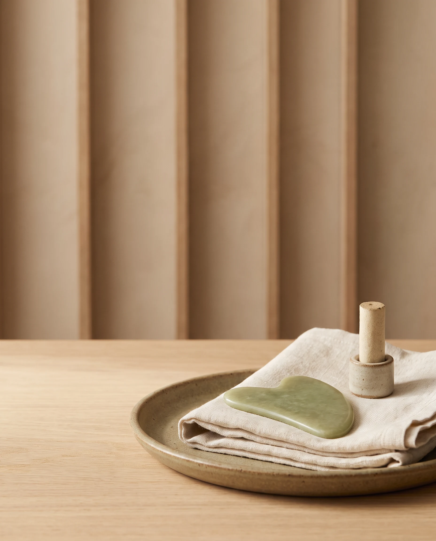 A pale jade gua sha tool and an unlit moxa roll arranged on natural linen.